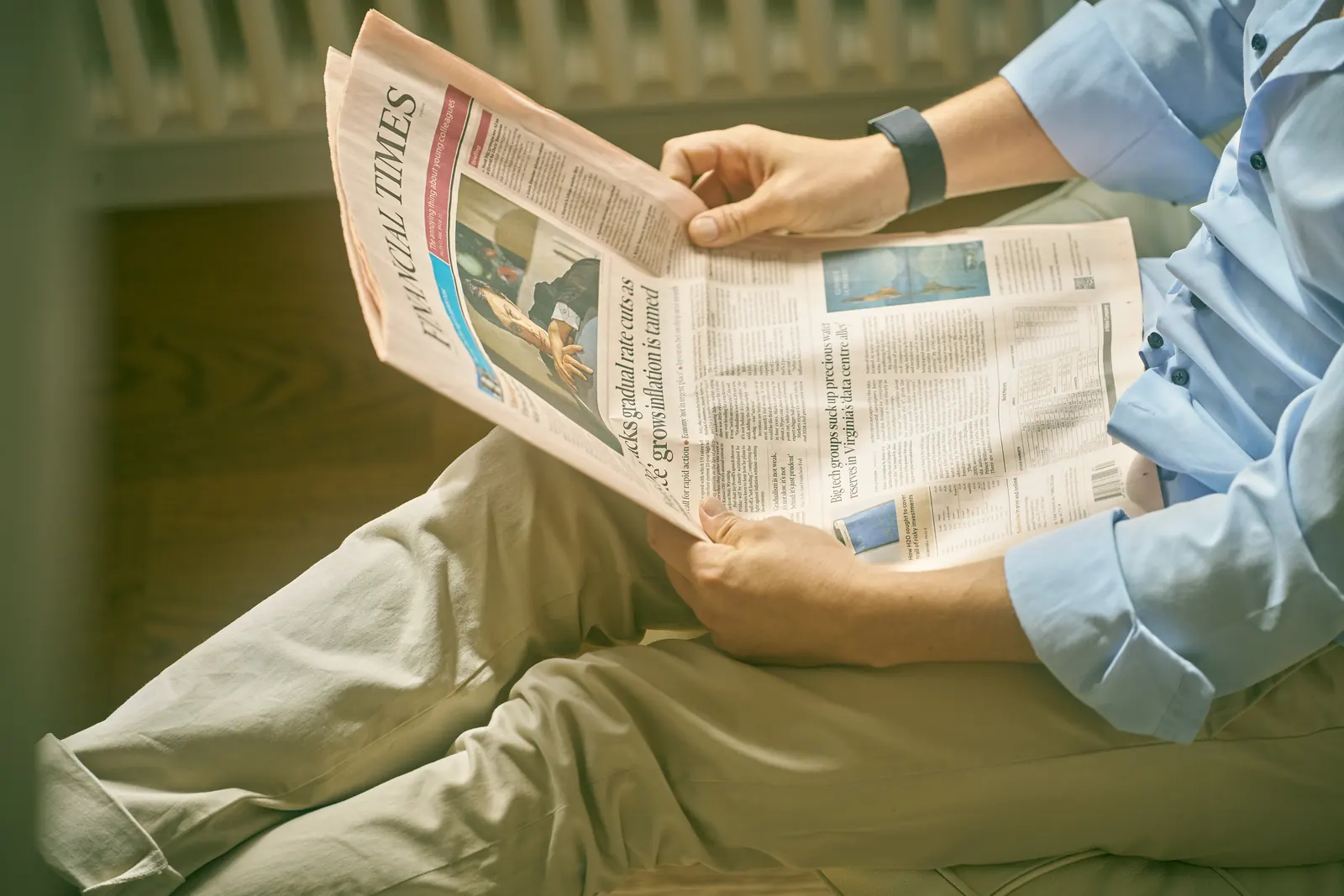 A person reads the Financial Times in a white leather lounge chair beside a window, face out of frame