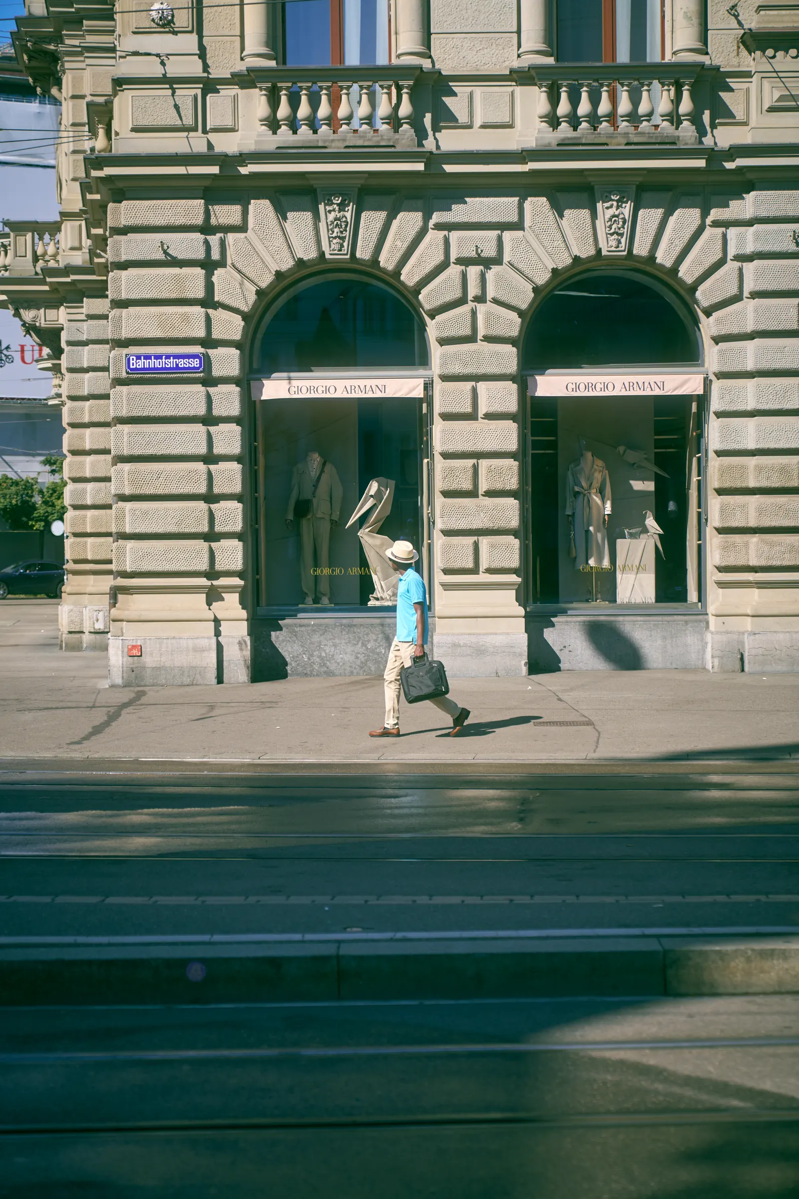 A passer-by walks past the arched windows of a stone bank building across tram tracks in Zurich