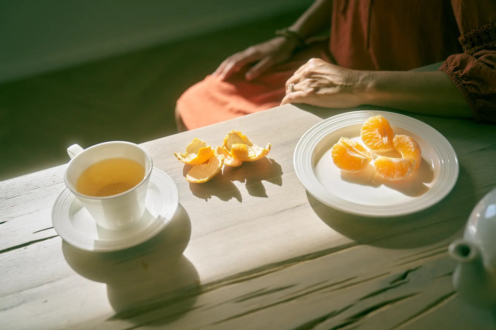 A cup of tea and peeled tangerine segments on a sunlit wooden table